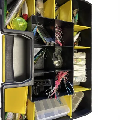 Black and yellow plastic tackle organizer filled with various fishing lures, jigs, bobbers, and accessories.