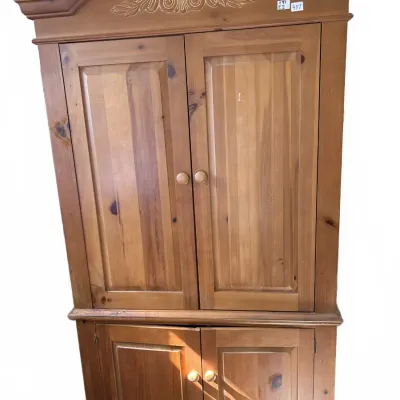 Pine corner armoire cabinet featuring a arched pediment with carved scroll accents and double panel doors on top and bottom.