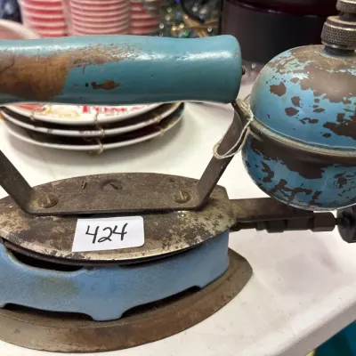 Vintage early 20th-century gas or liquid fuel pressing iron with light blue painted handle, base, and tank showing significant paint wear...