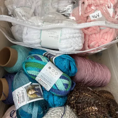 Assorted craft yarns including Red Heart Boutique Sashay ruffled ribbon yarn, textured chunky wool, and plush chenille skeins in a clear...