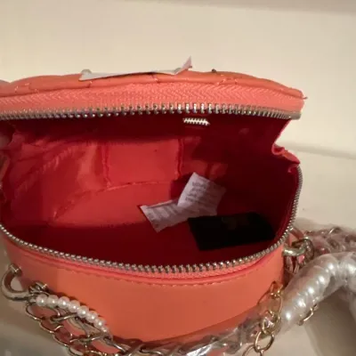 Open coral pink quilted round crossbody handbag featuring a zip-around closure, faux pearl strap accents, and gold-tone chain detail.
