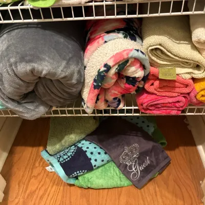 Assorted towels and plush blankets neatly stored on wire closet shelving and organized in a stack on the floor below.