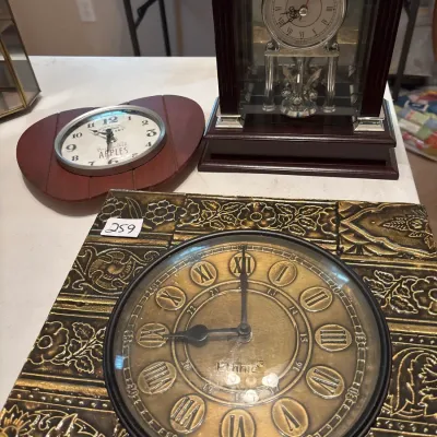 Collection of three decorative clocks, featuring a large brass-toned square wall clock with embossed scrollwork, a wooden mantel clock...