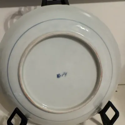 Underside of a Chinese blue and white porcelain plate displayed on a black easel stand, featuring a centered maker's mark and...
