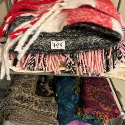 Stack of folded scarves and throw blankets with fringed edges stored on a metal drying rack.