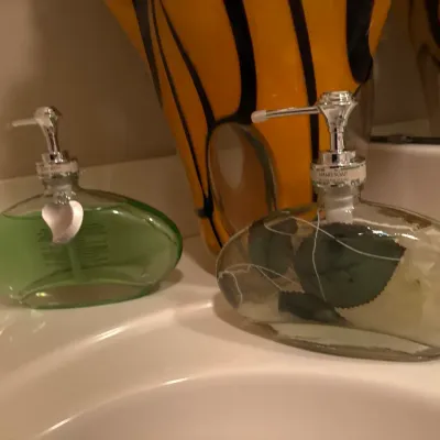 Pair of decorative glass soap dispensers with silver-tone pumps sitting beside a modern striped yellow and black vase on a bathroom counter.
