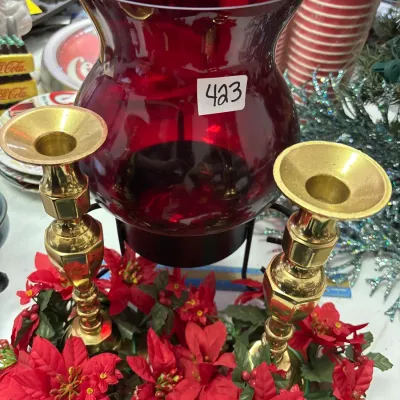 Holiday centerpiece featuring a large ruby red glass hurricane shade mounted on a metal base, paired with brass candlesticks and faux...