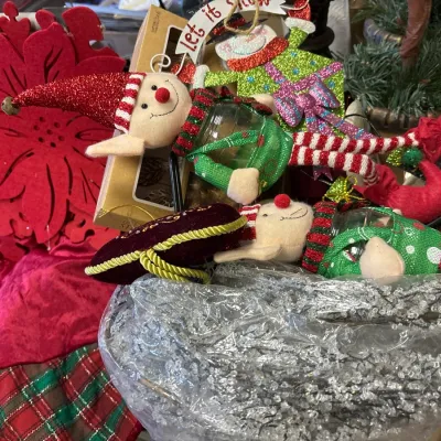 Collection of festive holiday decorations featuring plush elf and snowman ornaments, a felt poinsettia, silver beaded garland, and a...