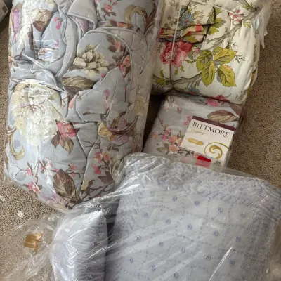 Collection of floral bed linens and decorative throw pillows, including packaged Biltmore drapery panels.
