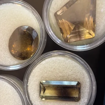 Collection of loose faceted smoky quartz gemstones in round display cases, featuring oval, freeform pentagon, and rectangular baguette cuts.