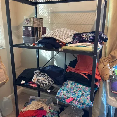 Black metal Origami folding four-tier shelving unit holding assorted folded clothing and boxed media.