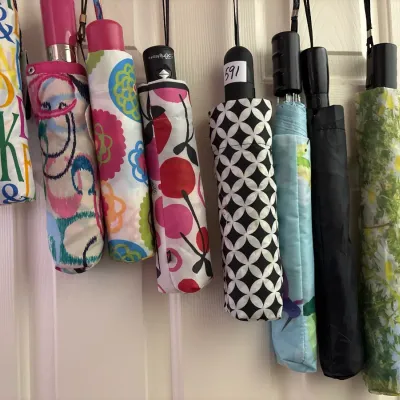 Collection of eight colorful compact travel umbrellas with various floral, geometric, and lettered patterns, hanging in a row.