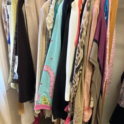 Wooden clothing rack filled with an assortment of women's sweaters, jackets, tops, and pants in various colors and patterns.