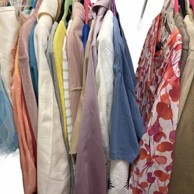 Selection of women's clothing, including blouses, jackets, and sweaters in various colors and patterns, hanging on a clothing rack.