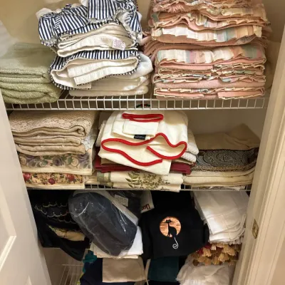 Linen closet filled with stacked bath towels, ruffled hand towels, floral linens, and decorative embroidered items.