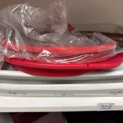 Stack of white ceramic baking dishes, including a floral patterned tray, topped with red silicone lids.