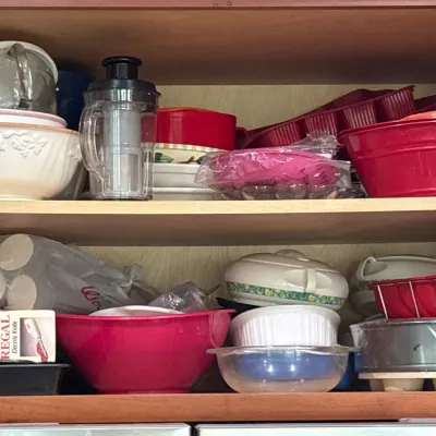 Assorted kitchenware stored in a cabinet, including colorful mixing bowls, silicone bakeware, glassware, and a small electric food...