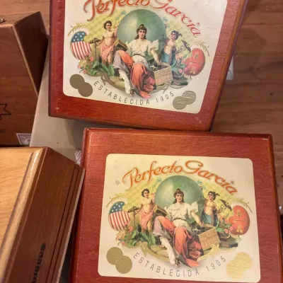 Two vintage Perfecto Garcia wooden cigar boxes featuring classic illustrated lid graphics with gold accents.
