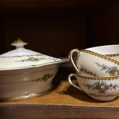 Vintage fine china covered tureen and stacked teacups with gilt rims and floral fruit basket motif.