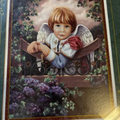 Framed artwork depicting a young cherubic angel leaning over a balcony surrounded by flowers, signed by artist Donna Richardson.
