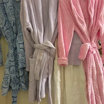 Selection of plush women's bathrobes hanging on a door frame, including patterned blue, solid lavender, and polka-dot pink styles.