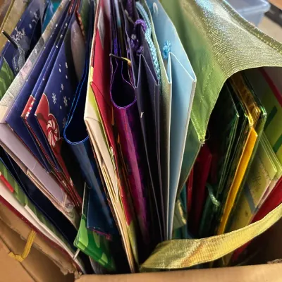 Large collection of colorful gift bags in various sizes, colors, and patterns, stored together in a cardboard box.