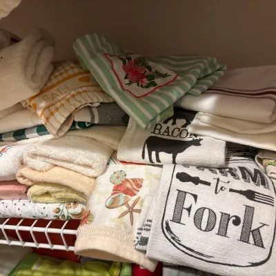 Large assortment of folded kitchen and hand towels with various seasonal and decorative prints, arranged on a wire closet shelf.