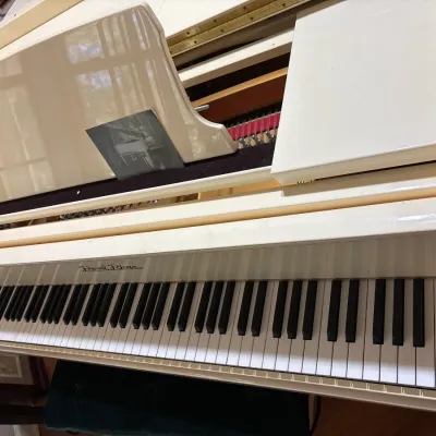 White high-gloss Pearl River baby grand piano featuring a music stand, key cover, and matching green velvet bench.