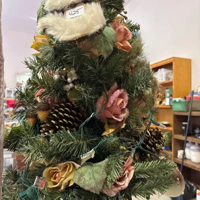 Small tabletop Christmas tree decorated with faux flowers, pinecones, strings of lights, and a plush Santa topper.