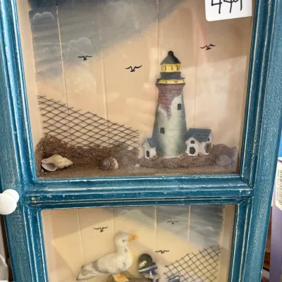 Rustic coastal shadow box cabinet featuring two glass panels with 3D lighthouse, seagull, and beach elements in a distressed teal wooden...