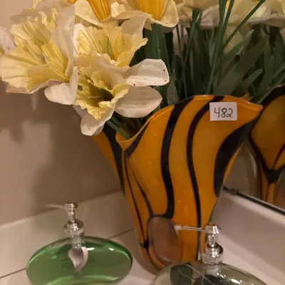 Arrangement of artificial yellow and white daffodils in a tiger-striped art glass vase, displayed alongside two liquid soap dispensers.