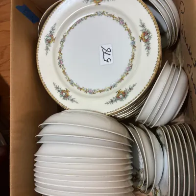 Cardboard box packed with a set of fine porcelain china dishware, featuring floral swag patterns and gold rim accents.