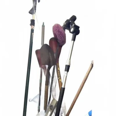 Assorted long-handled garden and cleaning tools, including a small shovel, a level, extension poles, and decorative yard stakes.