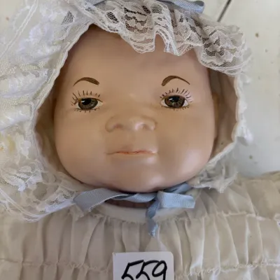 Vintage porcelain or composition baby doll featuring hand-painted facial details and wearing a lace-trimmed bonnet and gown.
