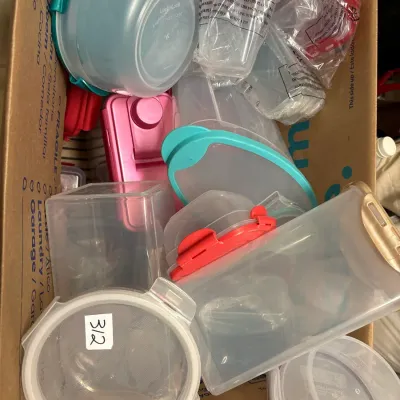 Cardboard moving box filled with various plastic food storage containers and lids including LocknLock brand items.