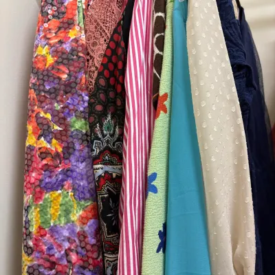 Selection of women's vintage and modern dresses hanging on a rack, featuring various patterns, sequined details, and textures.