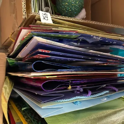 Box packed with assorted gift bags, wrapping supplies, and a green holiday ornament ball.