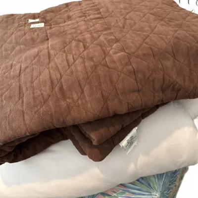 Folded brown quilted throw blanket stacked on top of white bedding linens.