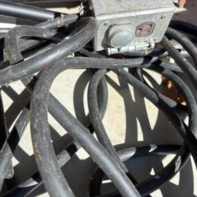 Heavy-duty black extension cord bundle attached to a metal electrical junction box with dual outlets.