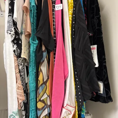 Closet rack packed with an assortment of women's vintage and contemporary tops, dresses, and blouses in various colors and patterns.