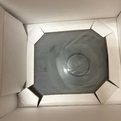 Clear glass bowl or dish packaged securely inside a cardboard shipping box with corner inserts.