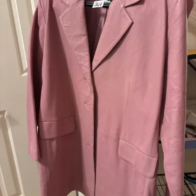 Vintage dusty pink leather blazer coat featuring wide notched lapels, front flap pockets, and a multi-button closure, hanging on a...