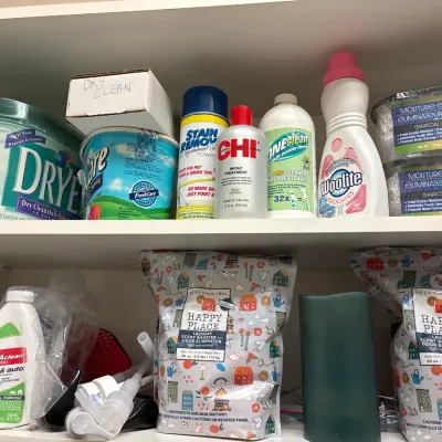 Assorted household cleaning products, laundry detergent, and stain removers arranged on white closet shelves.