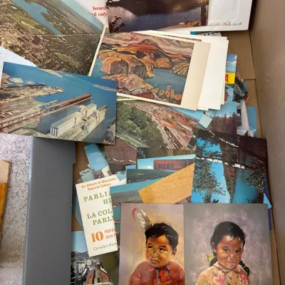 Large collection of vintage and mid-century postcards depicting landscapes, portraits, and scenic views, housed in a cardboard box.