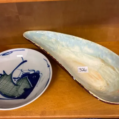 Two vintage ceramic serving pieces, including a round bowl with a blue and green fish design and an elongated light blue surfboard-shaped...
