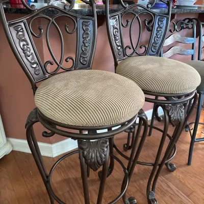 Pair of swivel barstools featuring dark bronze-tone wrought metal frames with scrollwork backs and round ribbed fabric seats.