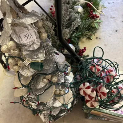Collection of Christmas decorations including a silver foil tabletop tree wrapped in string lights, a peppermint candy light strand, and...