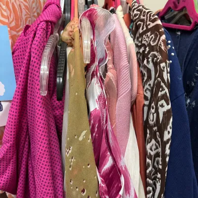 Selection of women's vintage and contemporary patterned tops and dresses hanging on a clothing rack.