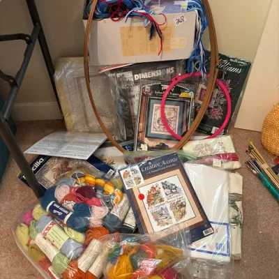 Collection of needlecraft supplies, including wooden and plastic hoops, needlepoint kits, embroidery canvas, and various colorful skeins...
