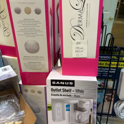 Selection of boxed home goods and personal care items, including a Sanus outlet shelf and DermaLuxe facial brush systems in original...